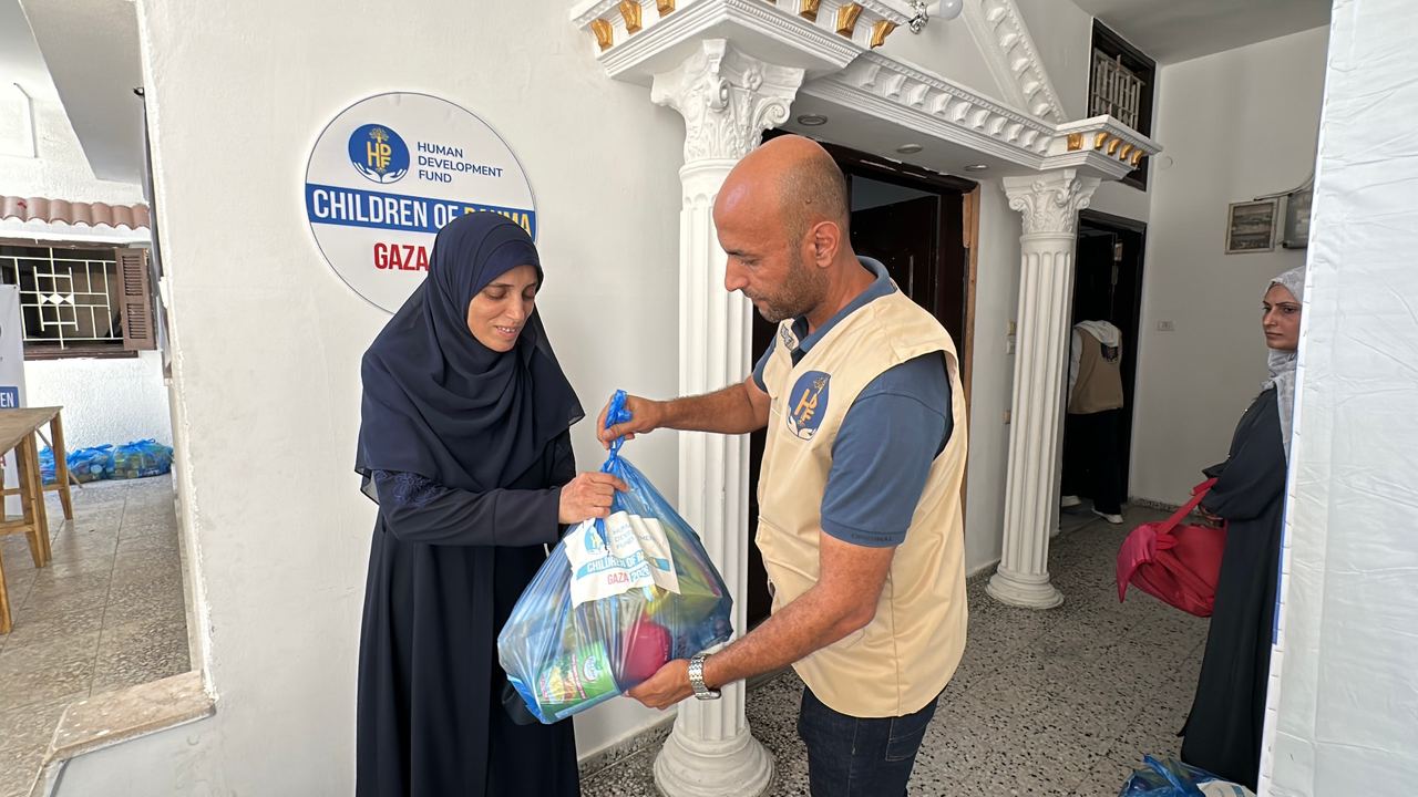 HDF field worker handing an HDF-labeled food parcel to a woman in Gaza during a distribution