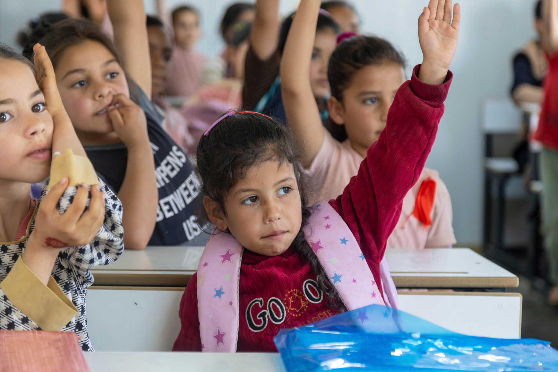 Children raising their hands at desks in an HDF-supported classroom in Gaza