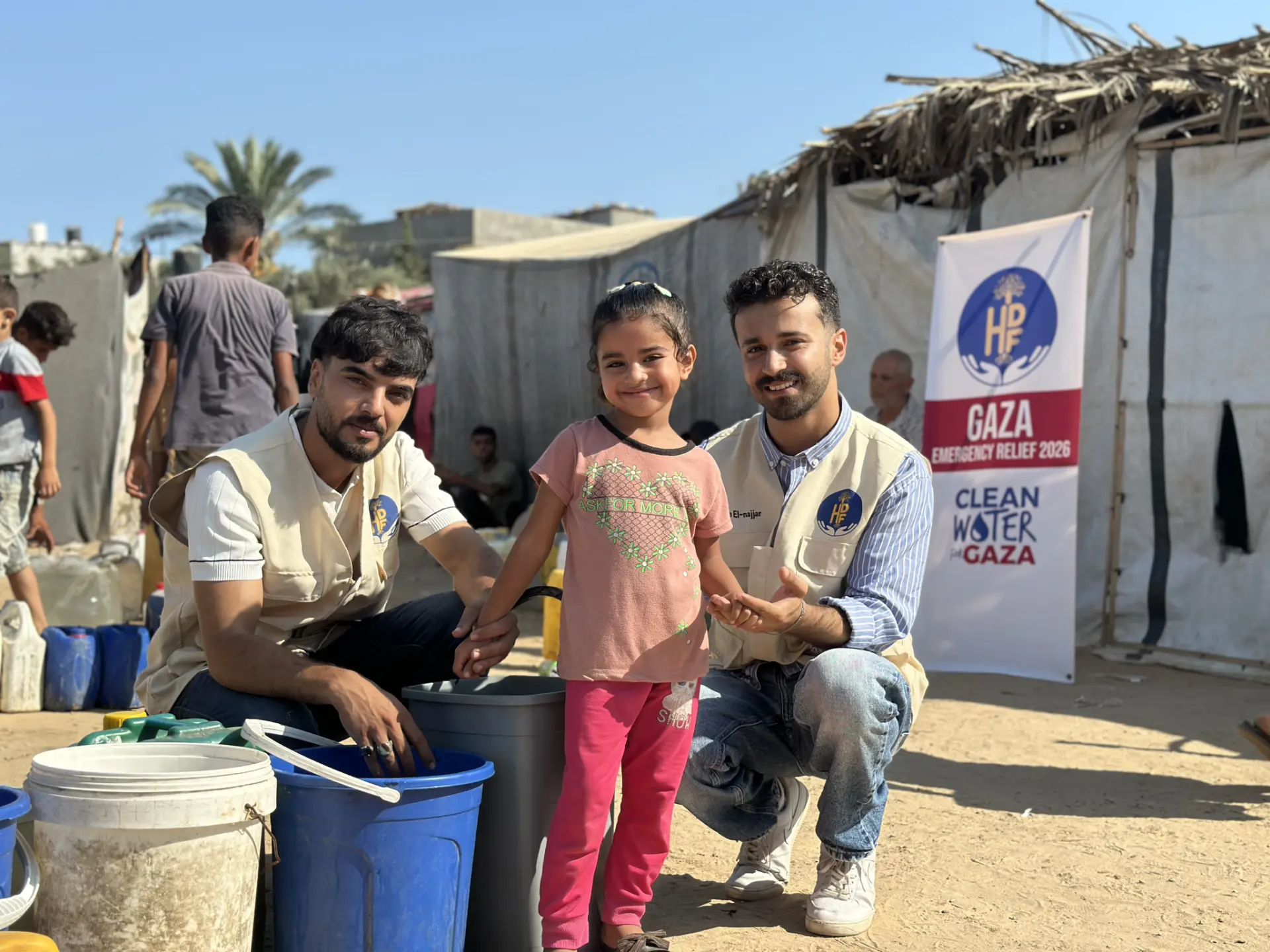 HDF field team with a child beside water buckets at a Clean Water for Gaza distribution point in a displacement camp