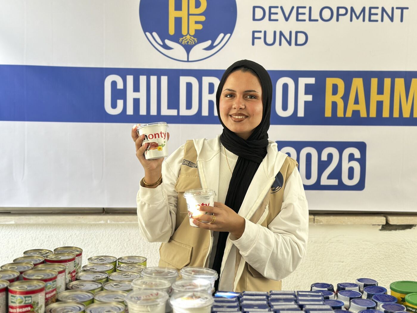 An HDF staff member holding canned food beside a Children of Rahma Gaza banner.