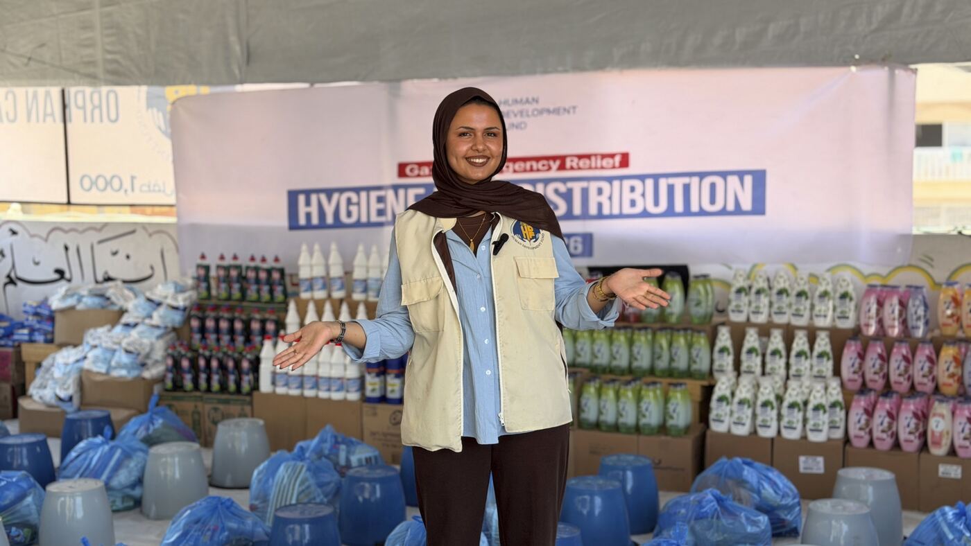 An HDF staff member standing among stacked hygiene supplies at a Gaza distribution point.