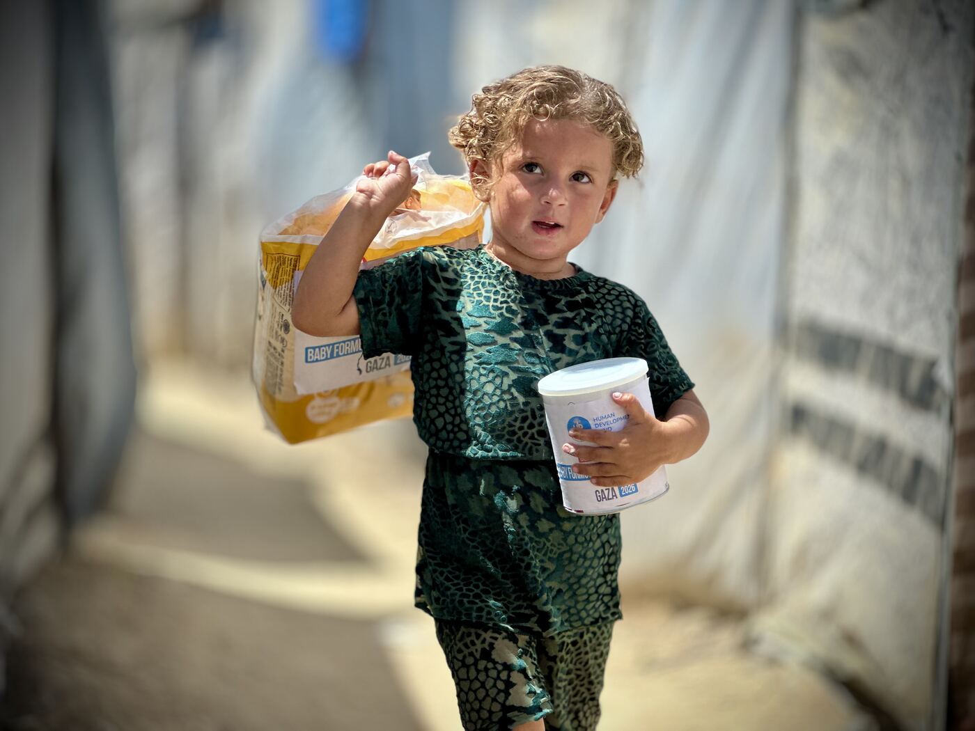 A young girl in Gaza holding a food container and packet.