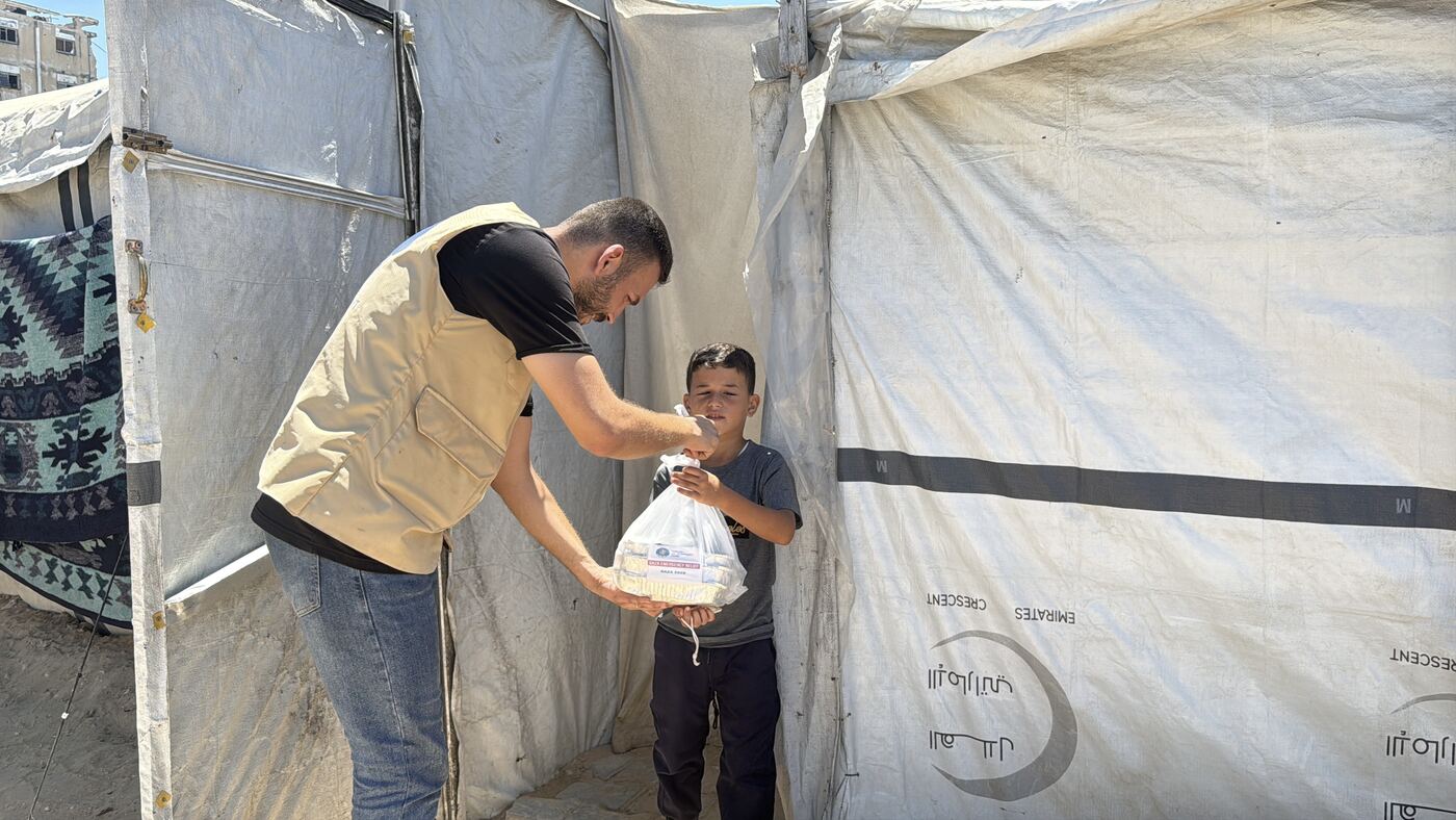 An HDF staff member handing a bagged food parcel to a boy outside a tent in Gaza.