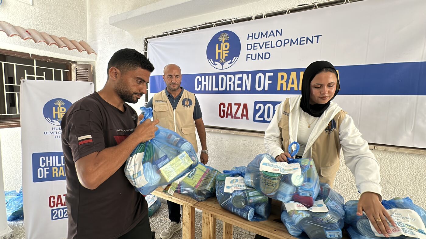 HDF staff sorting bagged food parcels on a table beneath a Children of Rahma Gaza banner.